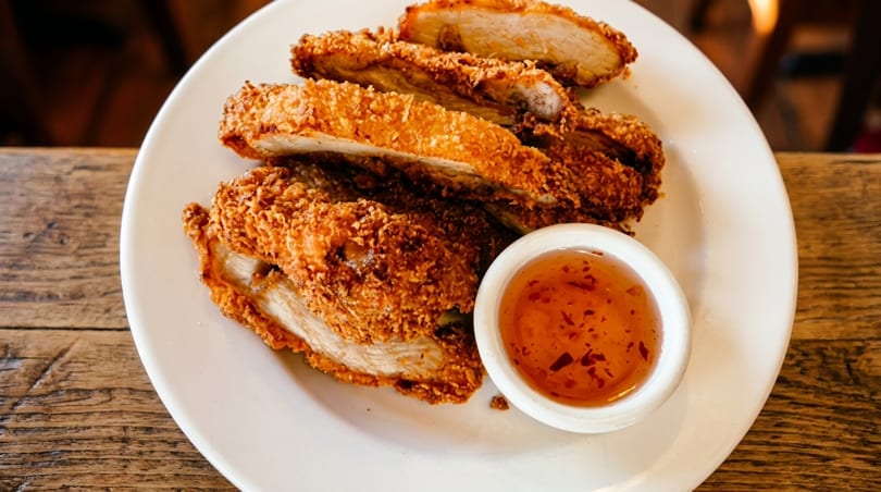 Crispy fried chicken pieces with a side of sweet chili dipping sauce on a white plate.