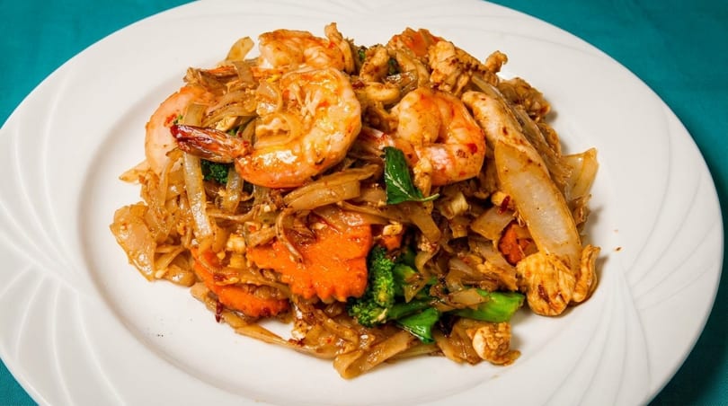 Pad See Ew with shrimp, chicken, broccoli, and carrots on a white plate.